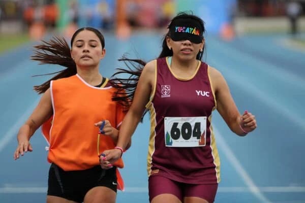 Atleta con uniforme de Yucatán corre junto a su guía en una pista de atletismo